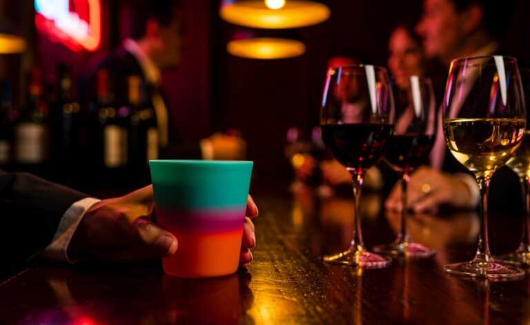 Illustration von einer stilvollen Weinbar, in der eine Hand einen bunten Silikonbecher hält, während im Hintergrund andere Gäste klassische Weingläser verwenden.